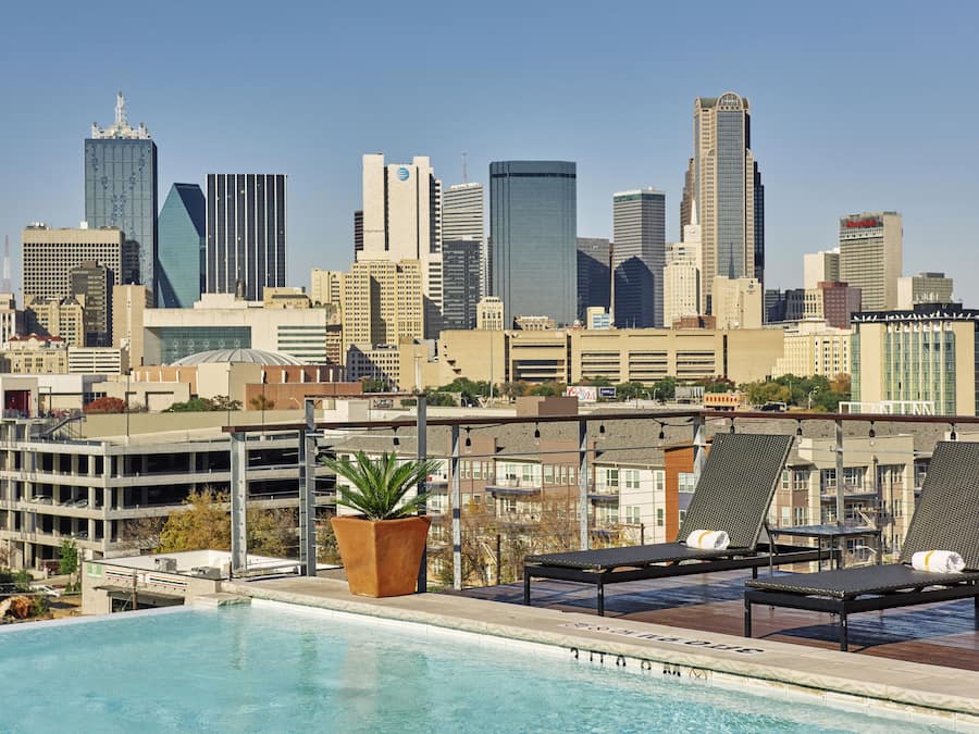 A rooftop pool with lounge chairs and a city skyline in the background.
