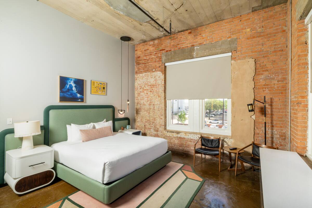 Ein Schlafzimmer mit Backsteinwand, einem Bett, einem Fenster, einem Schreibtisch und einem Stuhl.