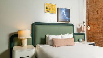 A hotel room with a green headboard, a bedside table with a lamp, a bed with white and pink pillows, and two framed pictures on the wall.