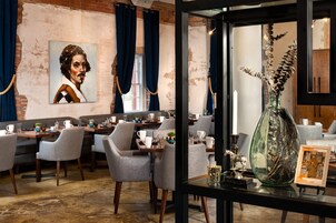 Un restaurant avec des tables dressées pour le service, un grand portrait accroché au mur et un vase décoratif posé sur une table.
