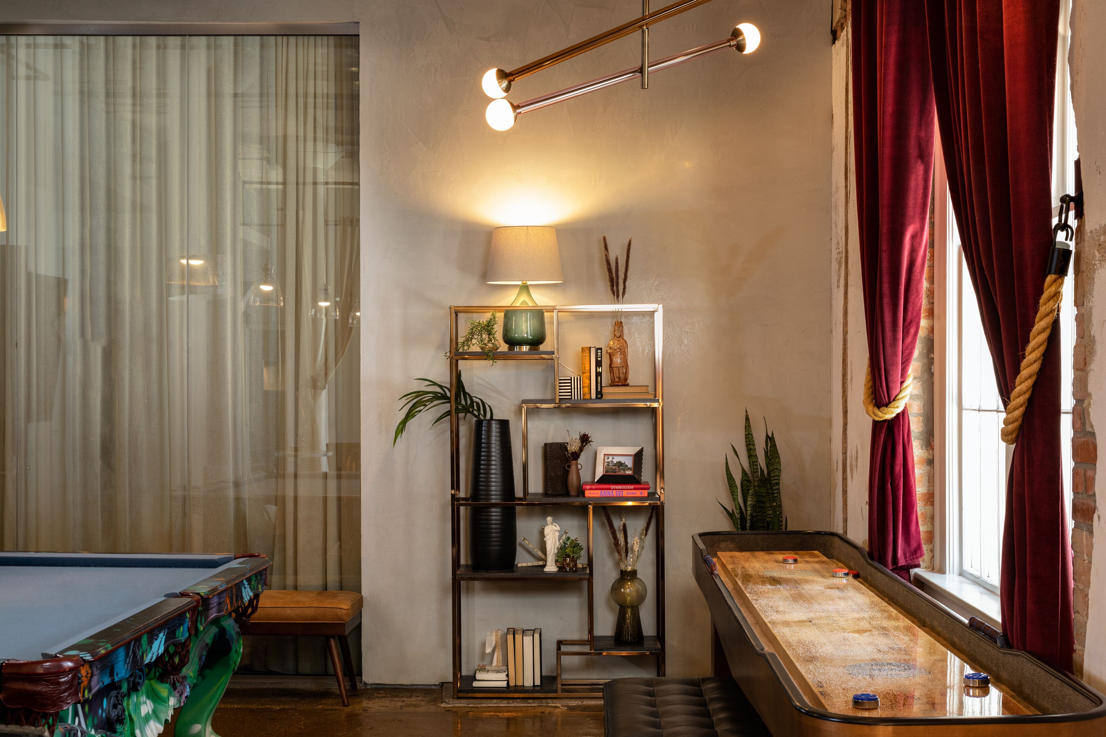 Uma mesa de bilhar, uma estante de livros e uma janela com cortinas.