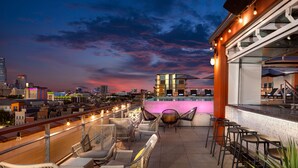 A rooftop bar with wicker chairs and tables, overlooking a cityscape at dusk. - Canvas Hotel Dallas (Dallas)