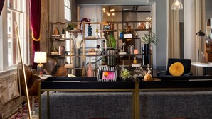 A modern living room with a sofa, red ottomans, a bookshelf, and a lamp. - Canvas Hotel Dallas (Dallas)