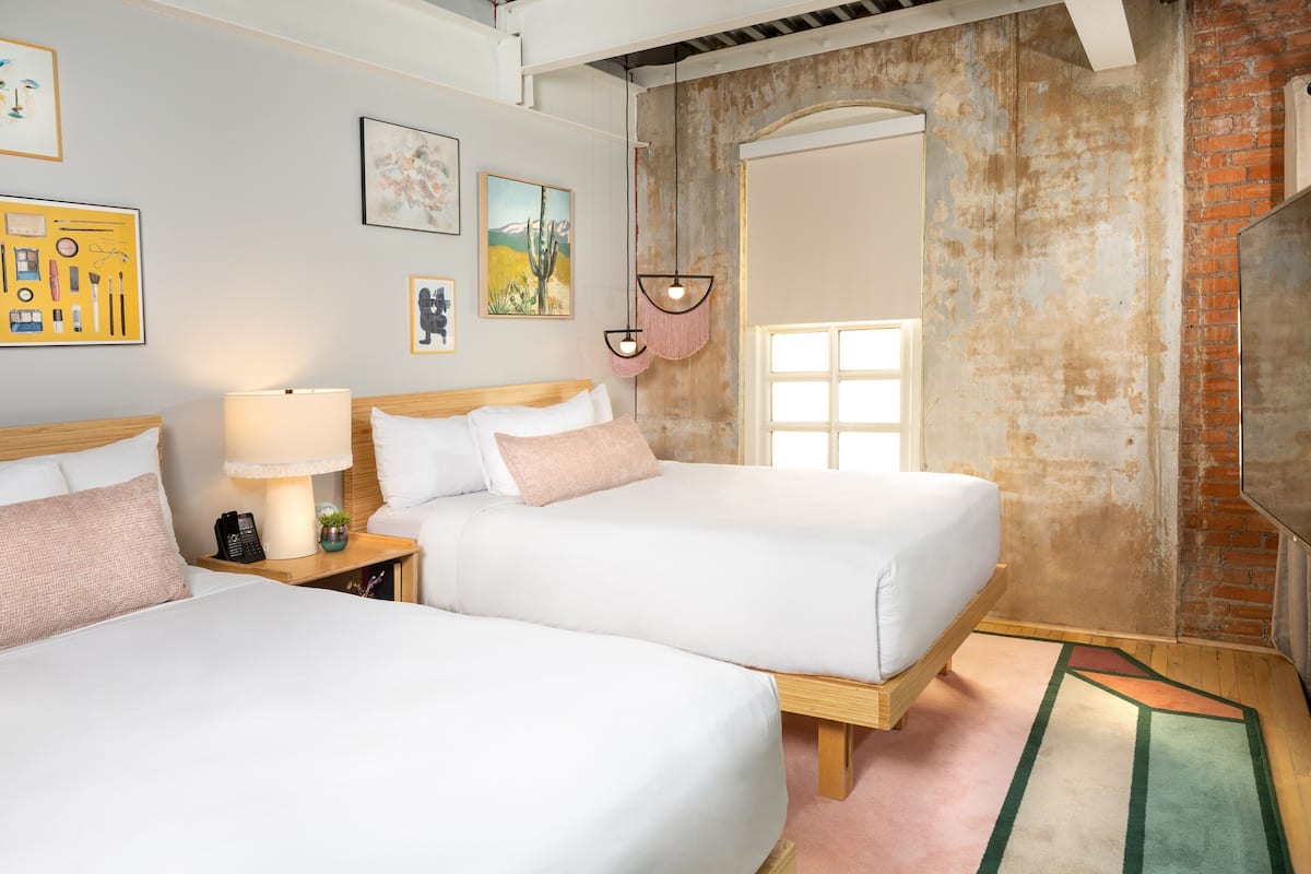 A hotel room with two beds, a lamp, a phone, and artwork on the walls.