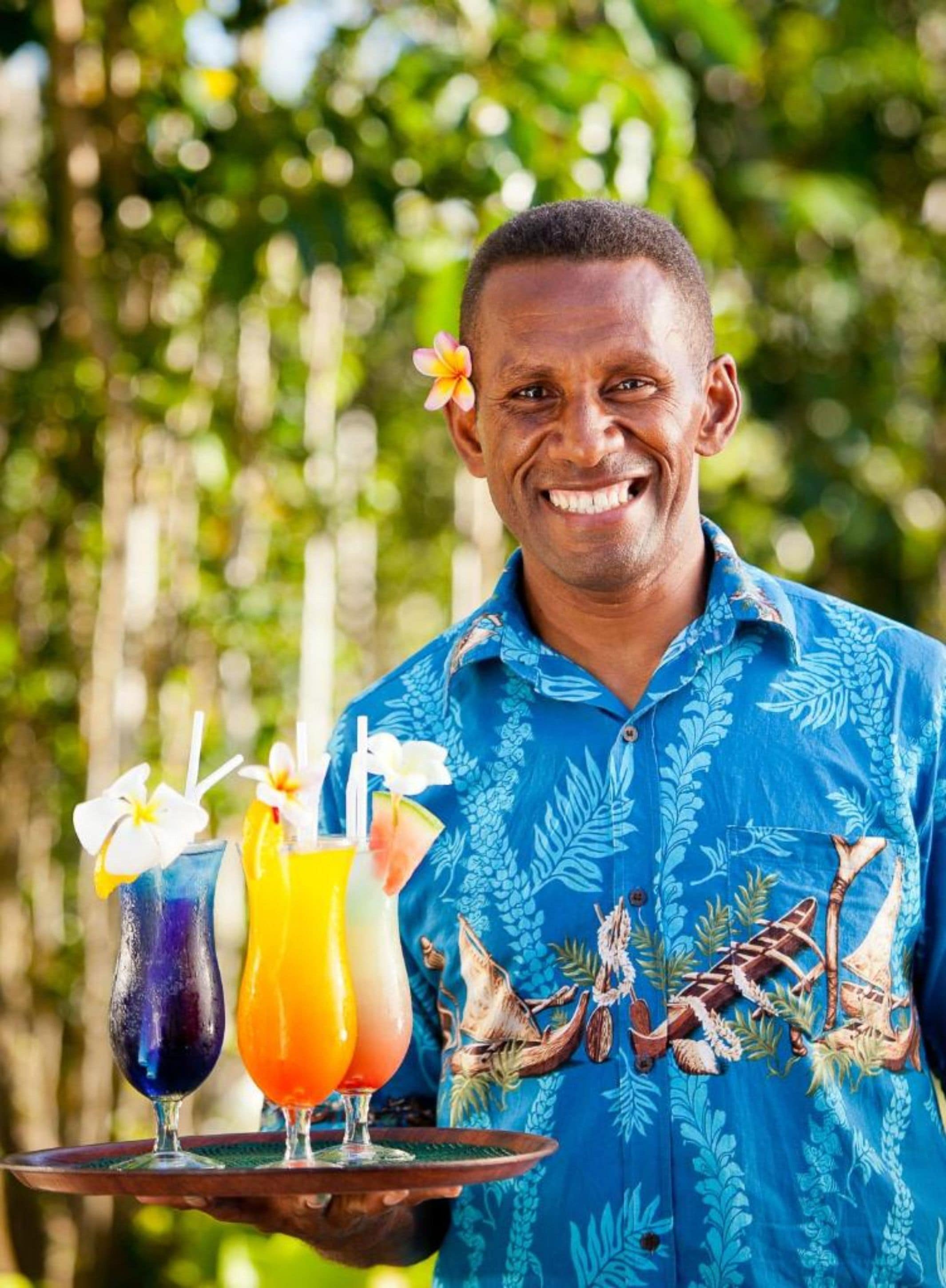 A person holding a tray with two drinks and a flower.