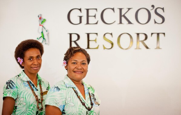 Two individuals standing in front of a sign that reads "GECKO'S RESORT".
