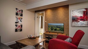 A living room with a wooden coffee table, a red armchair, and a flat-screen TV on a wooden stand. - Ons Epen (Epen)