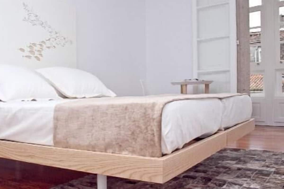 Ein modernes Schlafzimmer mit einem Bett auf einer Holzplattform, weißer Bettwäsche und einem dekorativen Wandbild.