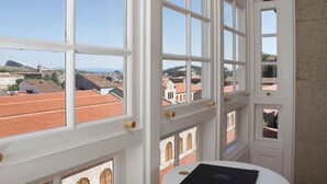 A room with large windows offering a view of red-roofed buildings and a distant landscape.