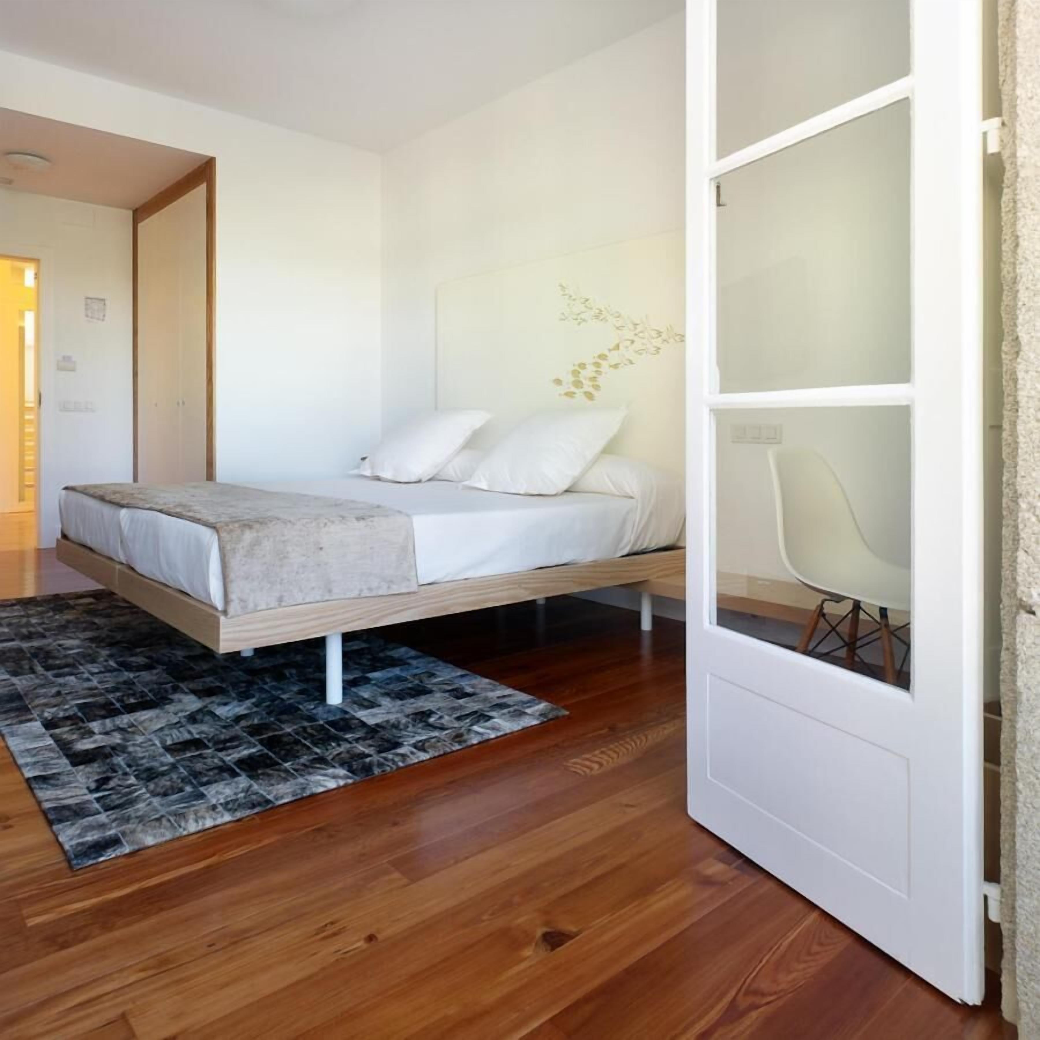 A bedroom with a bed, a rug, a chair, and a door.