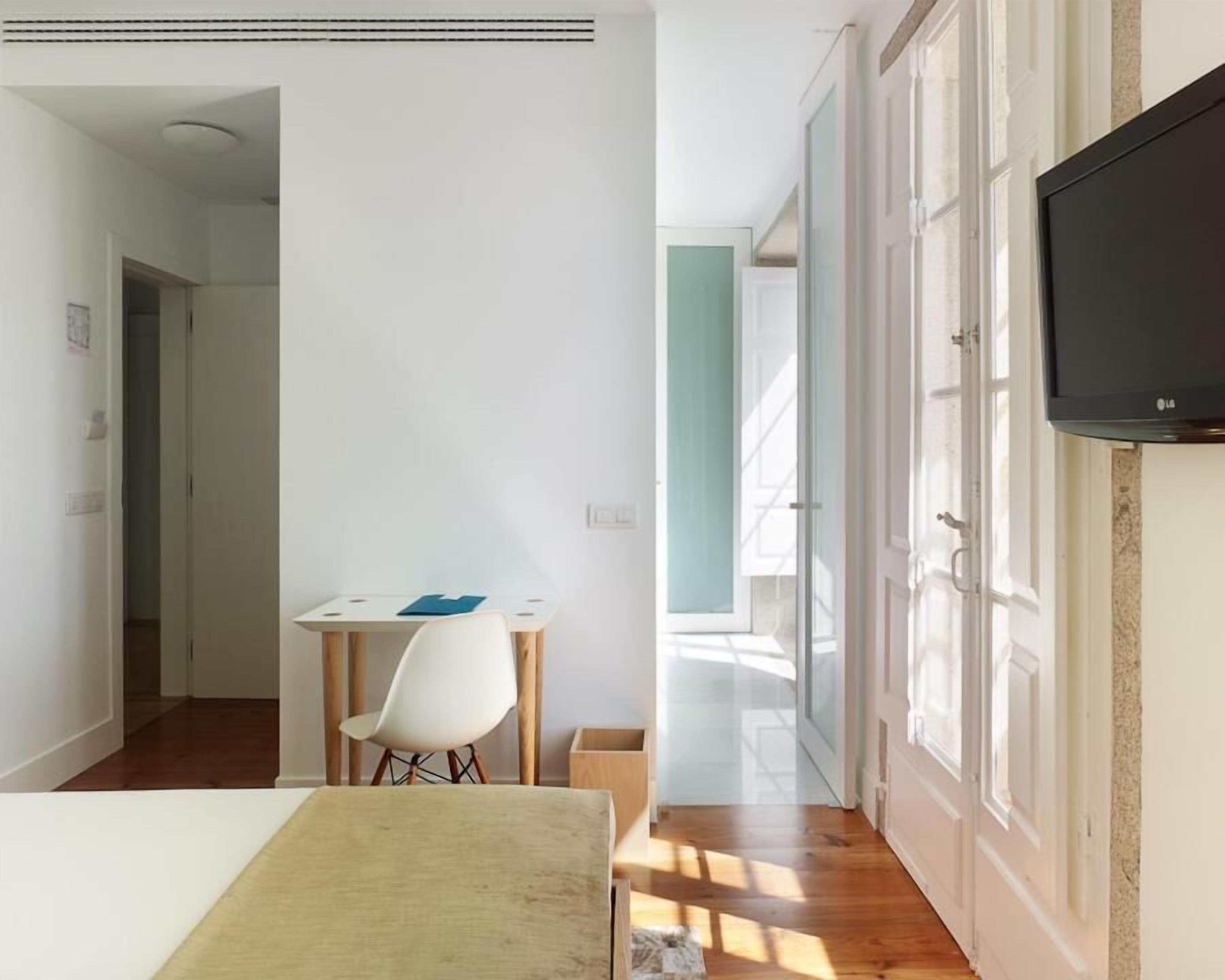 Een kamer met een houten vloer, een witte tafel met een blauwe placemat, een witte stoel en een televisie aan de muur.