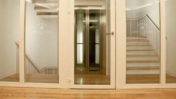 Entrada de un hotel con puerta de cristal, escalera de madera y un logotipo visible en la pared.