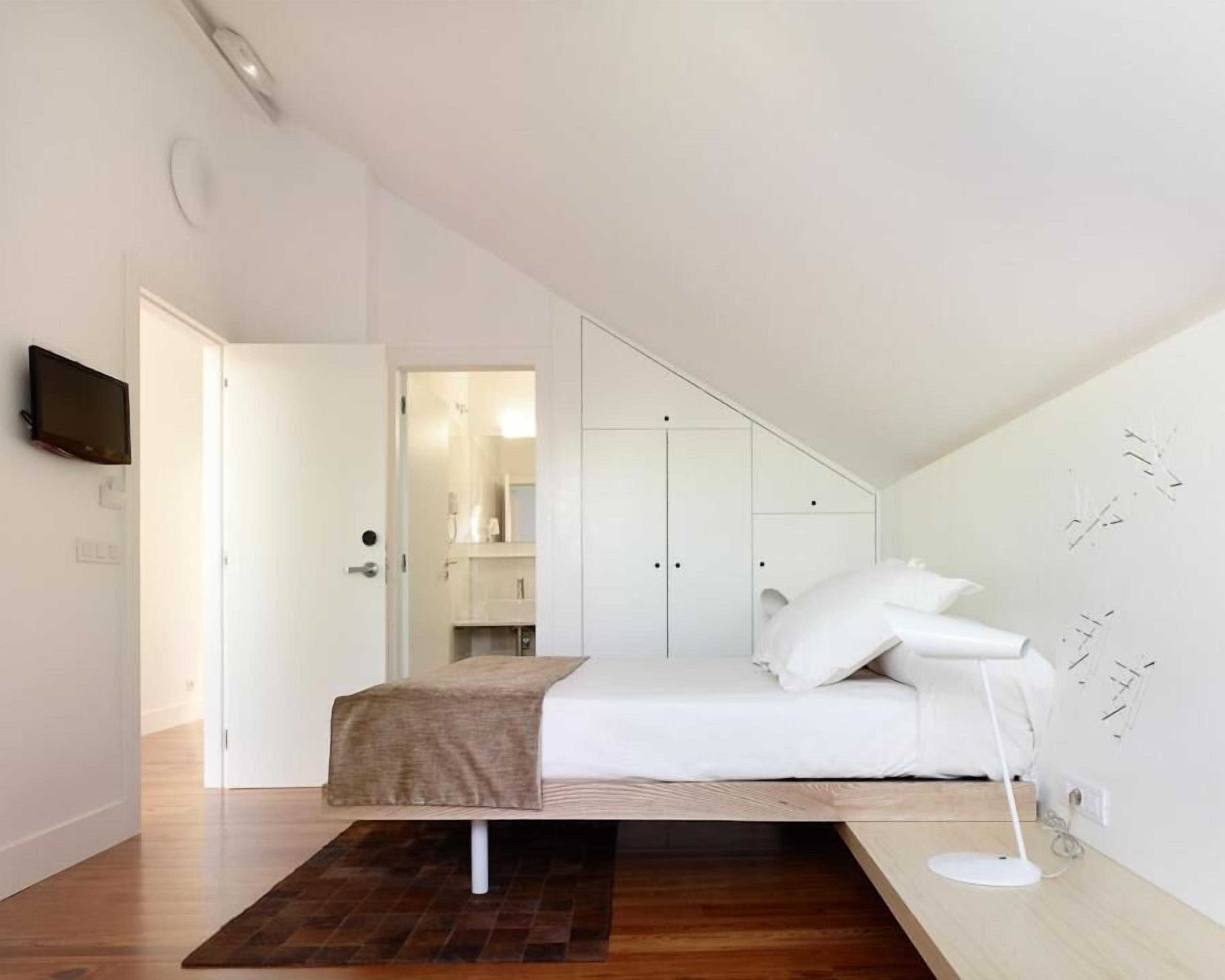 A bedroom with a bed, a bedside table, a lamp, and a wall-mounted TV.