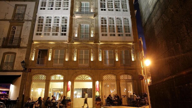 A historic building with multiple balconies and large windows, featuring a ground-floor restaurant with outdoor seating.