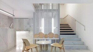 A modern interior with a marble reception desk, a round table with chairs, and a staircase.