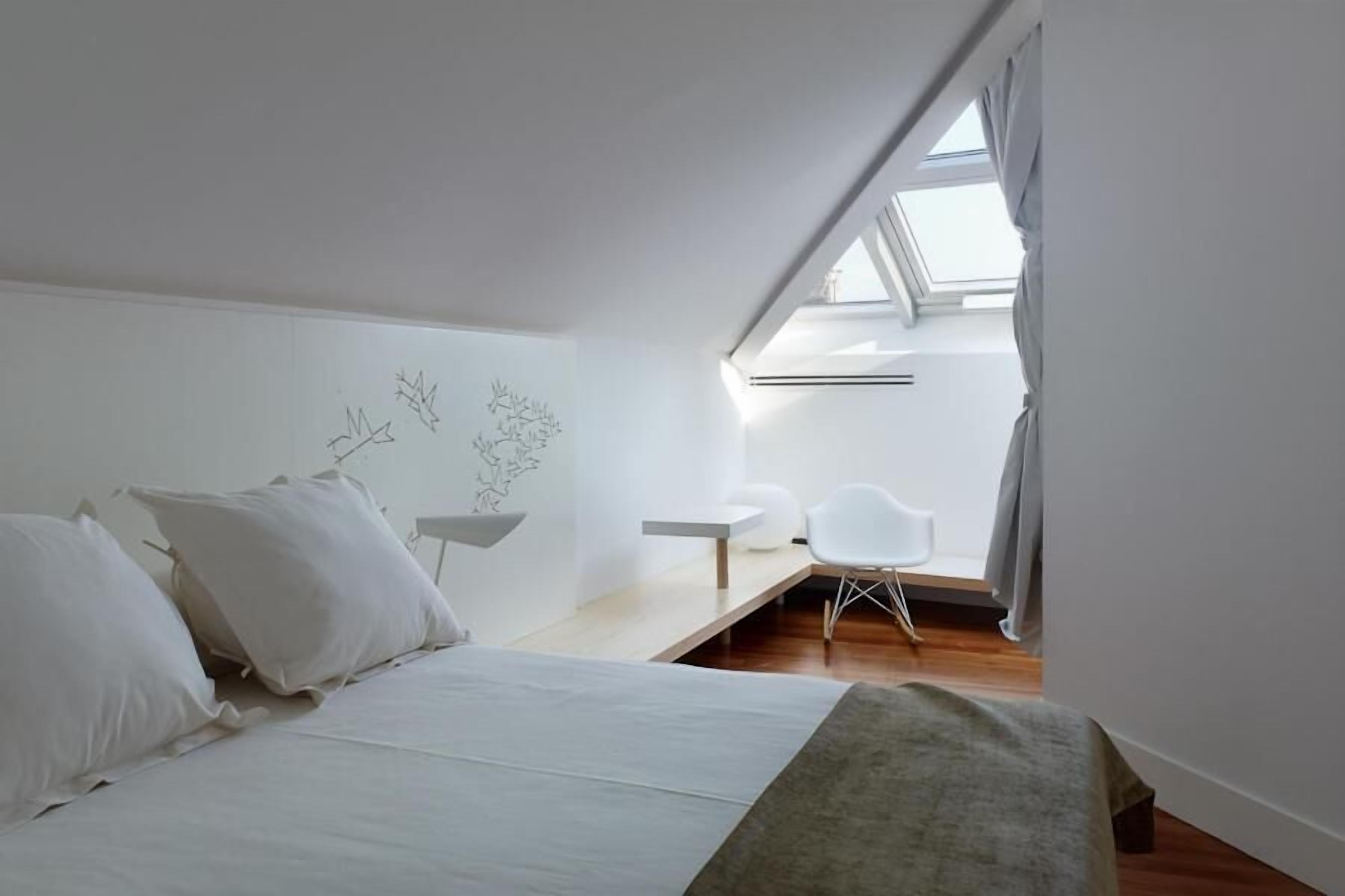 A bedroom with a bed, a desk, a chair, and a skylight.