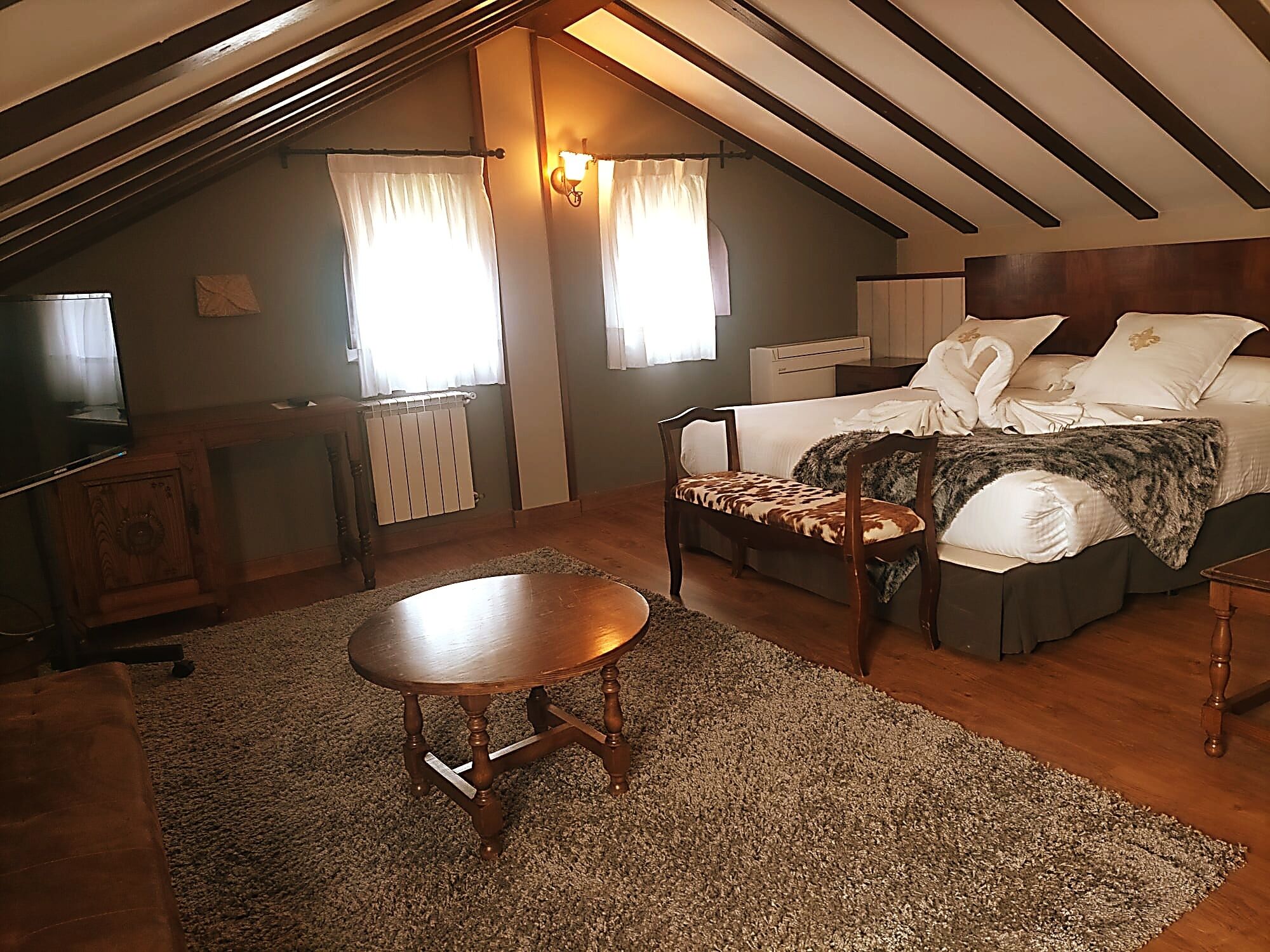 A cozy attic bedroom with a bed, a wooden chair, a small table, and a radiator.