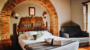 A bedroom with a brick arched headboard, a bed with white linens, a black sofa, and two wall-mounted lamps. - Posada San Marcos (Santillana del Mar)