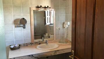 Un baño con lavamanos de mármol, espejo, secador de pelo y toallero.