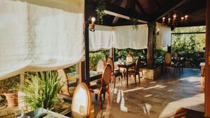 An outdoor dining area with wooden tables and chairs, covered by white cloths, and surrounded by potted plants and greenery. - Posada San Marcos (Santillana del Mar)
