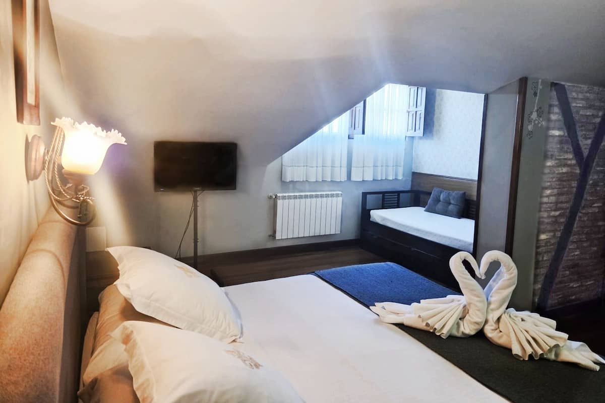 Quarto de hotel com cama, televisão presa à parede, radiador e janela com cortinas.