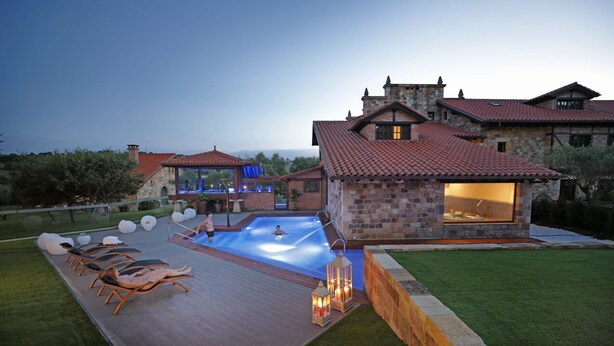 A poolside area with lounge chairs, a swimming pool, and a stone building with a tiled roof. - Posada San Marcos (Santillana del Mar)