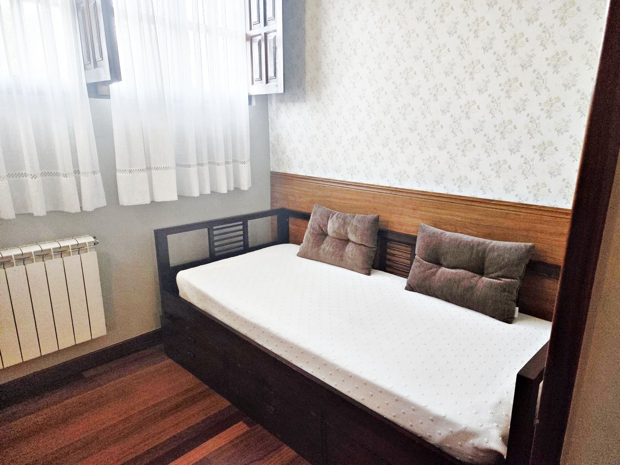 A small, single-bed room with a wooden headboard, white bedding, and a radiator below the window.
