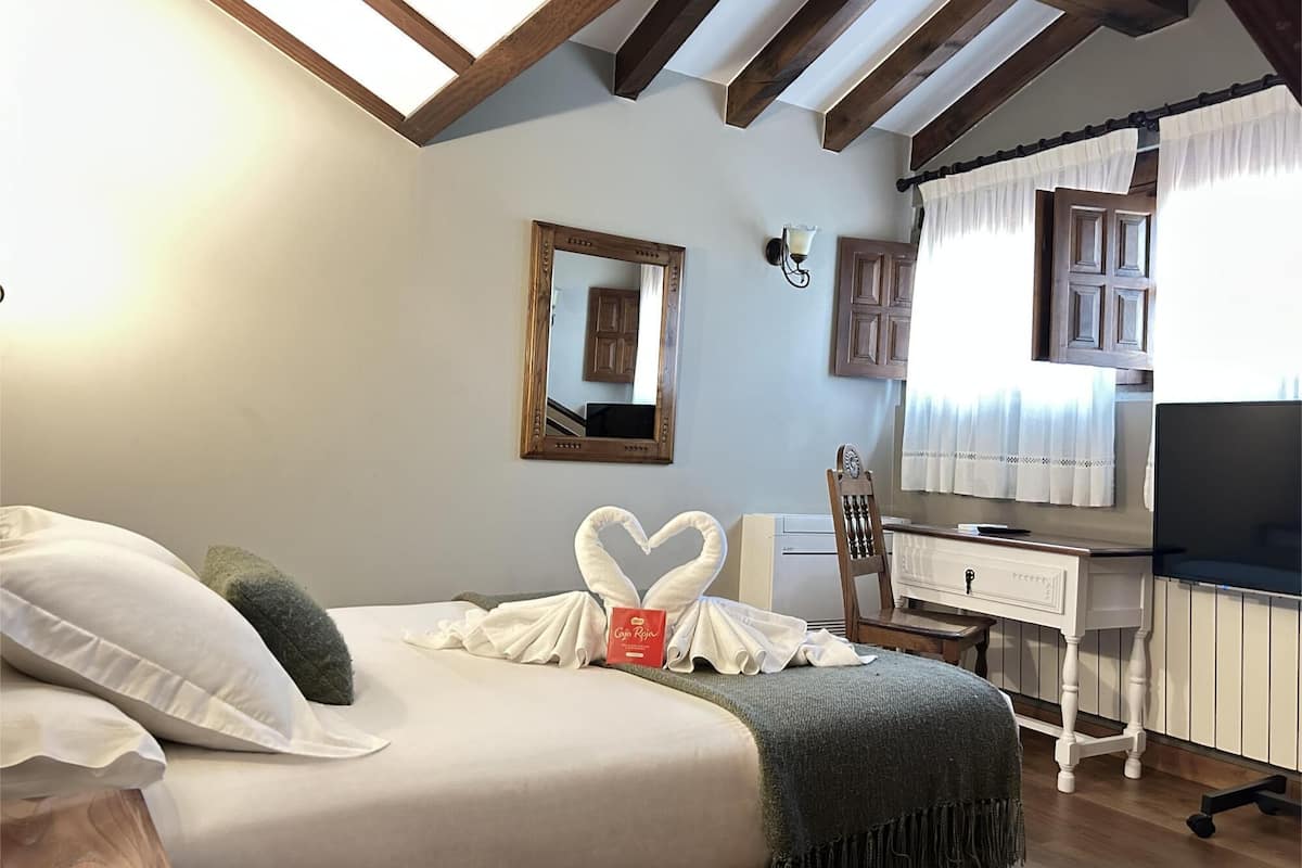 Quarto com cama, escrivaninha, cadeira, espelho e televisão.