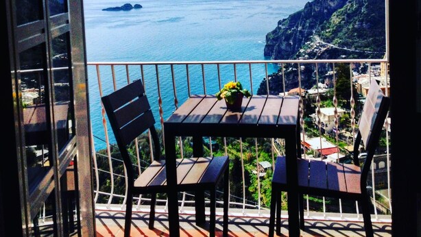 A balcony with a table and chairs overlooking a coastal view. - Bed & Breakfast Mamma Rosa (Positano)