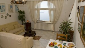 A living room with a sofa, dining table with breakfast, and a large window with curtains. - Bed & Breakfast Mamma Rosa (Positano)