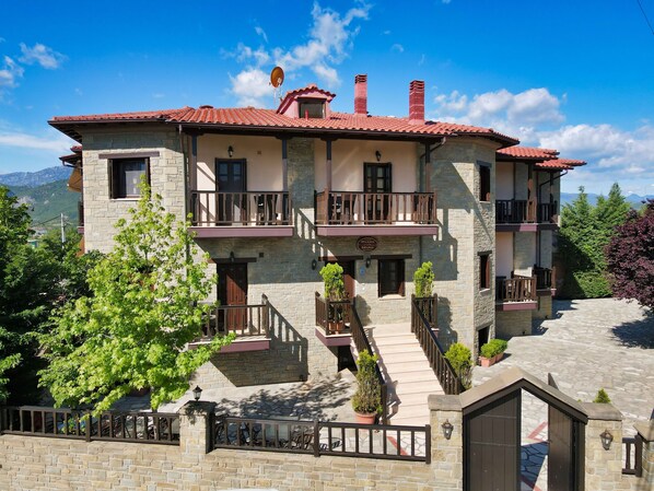 A two-story stone building with balconies, a stone staircase, and a view of mountains. - Iridanos (Kalabaka)