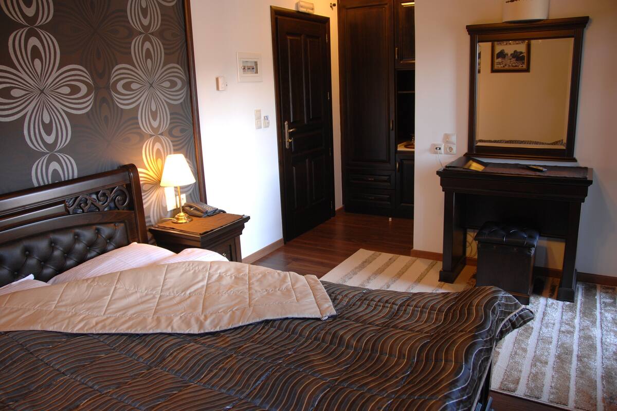 A hotel room with a bed, a nightstand, a lamp, a dresser, and a mirror.