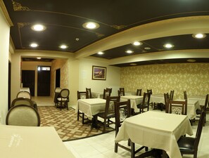 A restaurant with multiple tables and chairs, a patterned floor, and a dark ceiling with recessed lighting. - Iridanos (Kalabaka)