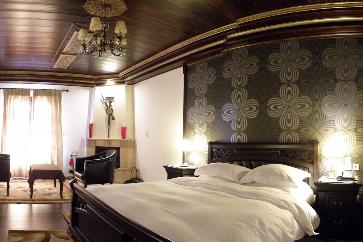 A hotel room with a large bed, a desk with a chair, a vanity with a mirror, and a patterned wallpaper.