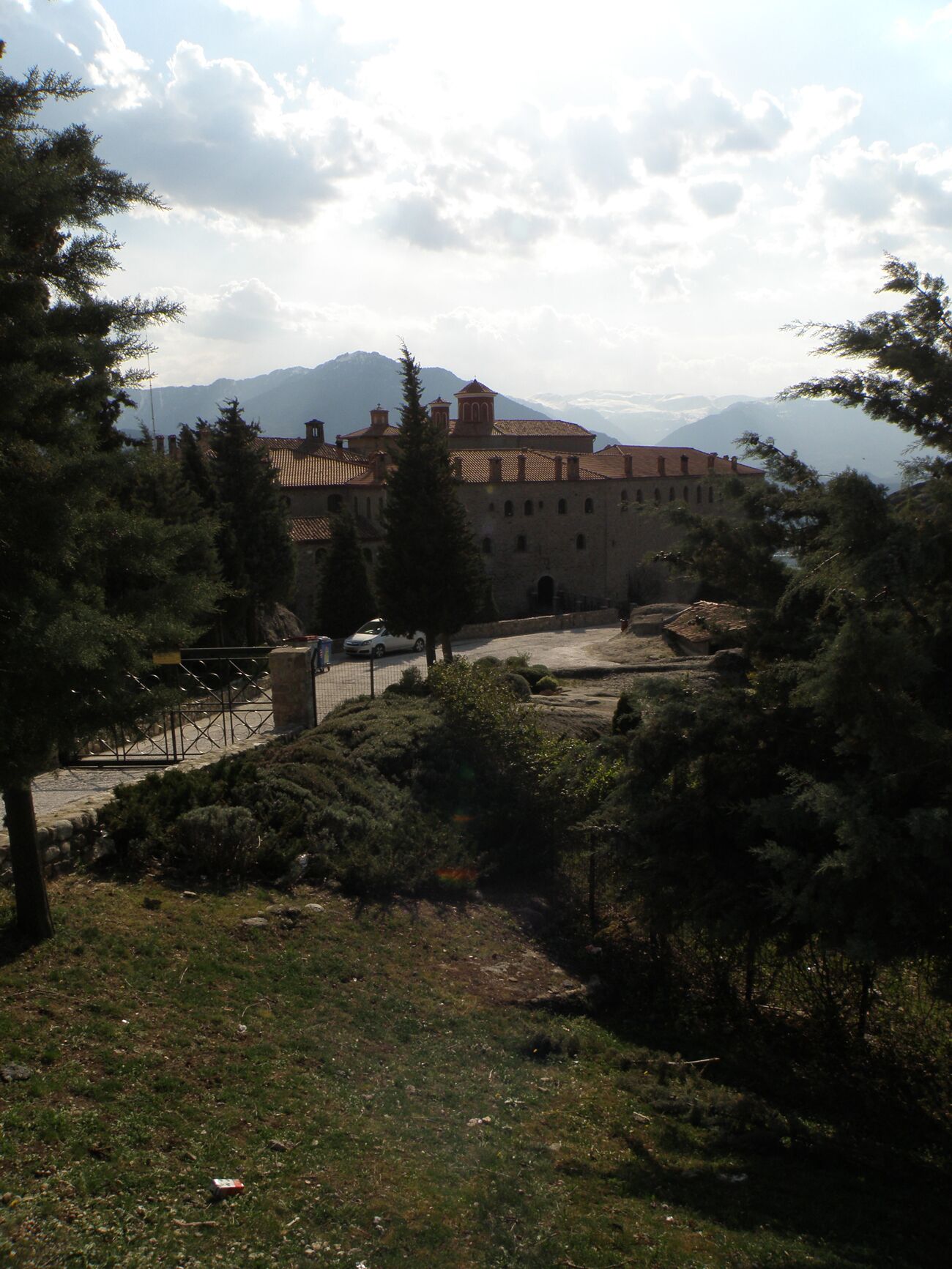 Un edificio histórico con un patio interior, rodeado de árboles y montañas al fondo.