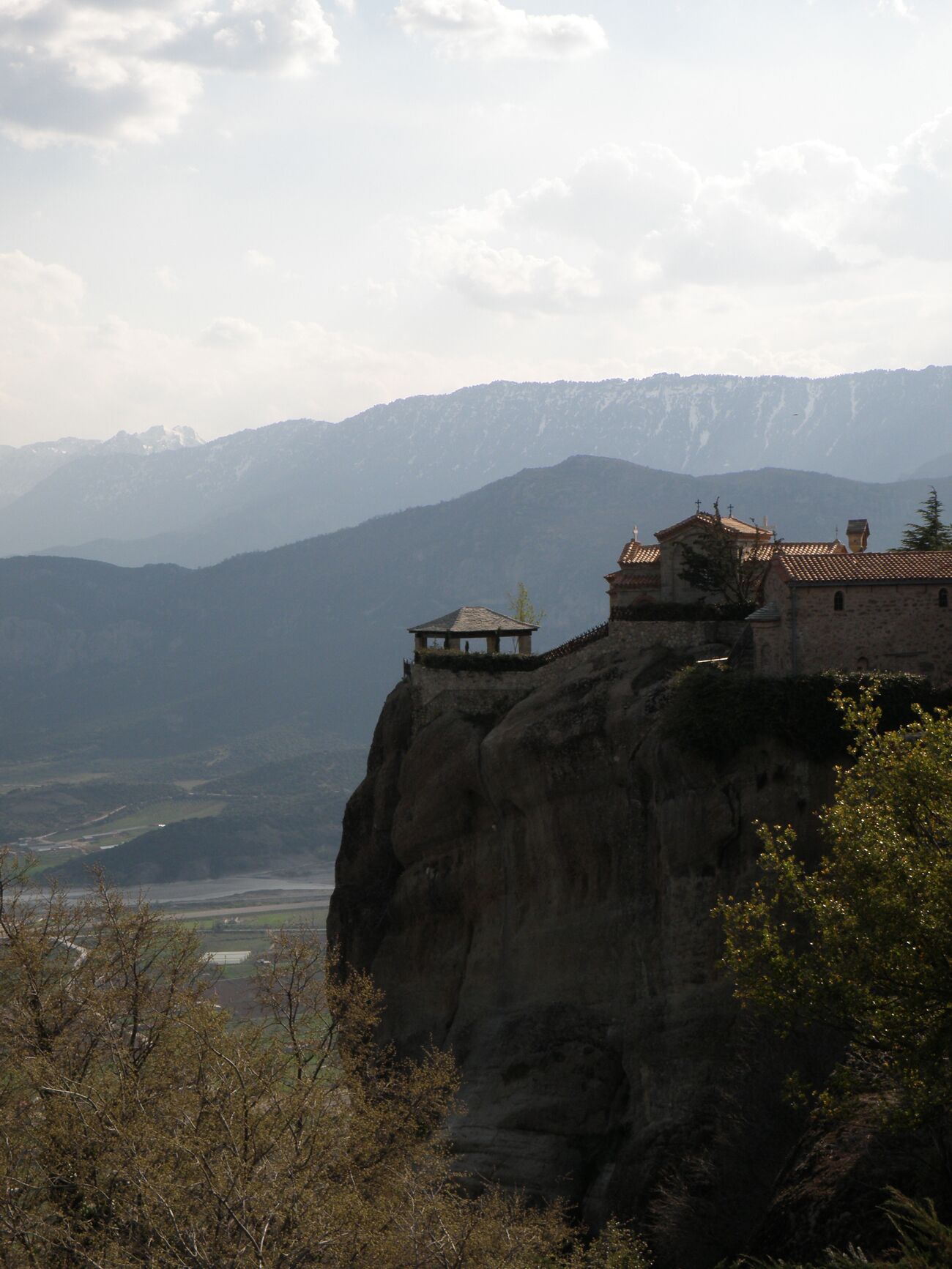 A monastery perched on a cliff with a view of distant mountains.