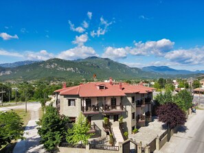 A multi-story building with a red-tiled roof, balconies, and a view of mountains in the background. - Iridanos (Kalabaka)