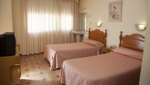 A hotel room with two beds, a sink, a mirror, a television, and a painting on the wall. - Hostal París (La Línea de la Concepción)