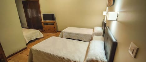 A small, well-lit room with two single beds, a wooden cabinet with a television, and a wardrobe.