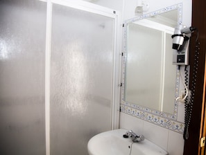 Un baño con lavamanos blanco, un espejo con marco decorativo y un secador de pelo en la pared.