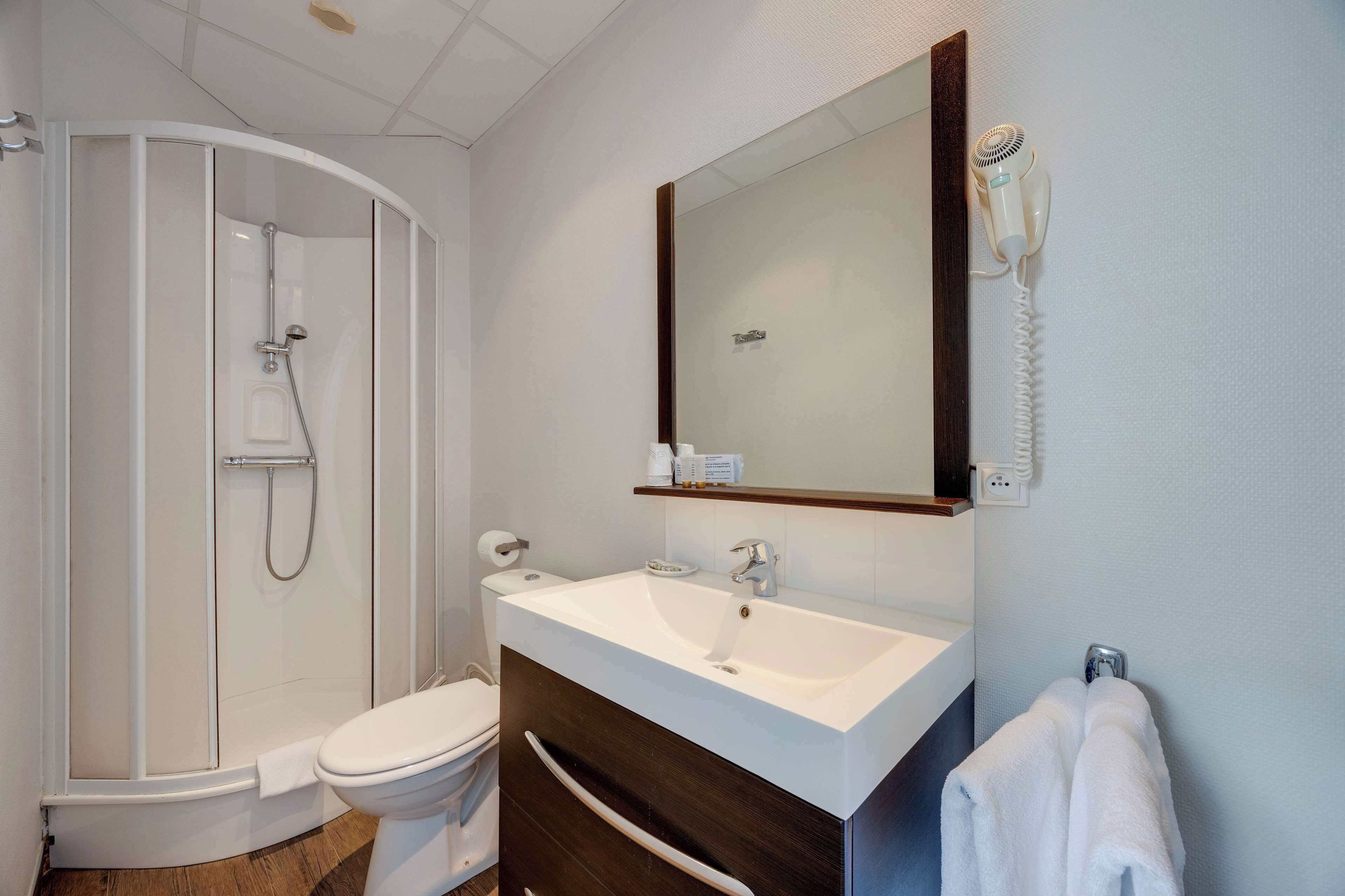 Un baño con ducha, inodoro, lavabo y espejo con secador de pelo.