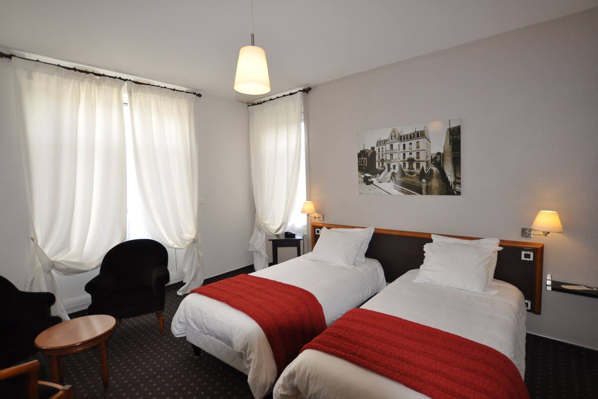 Een hotelkamer met twee bedden, een stoel, een tafel en een wandlamp.