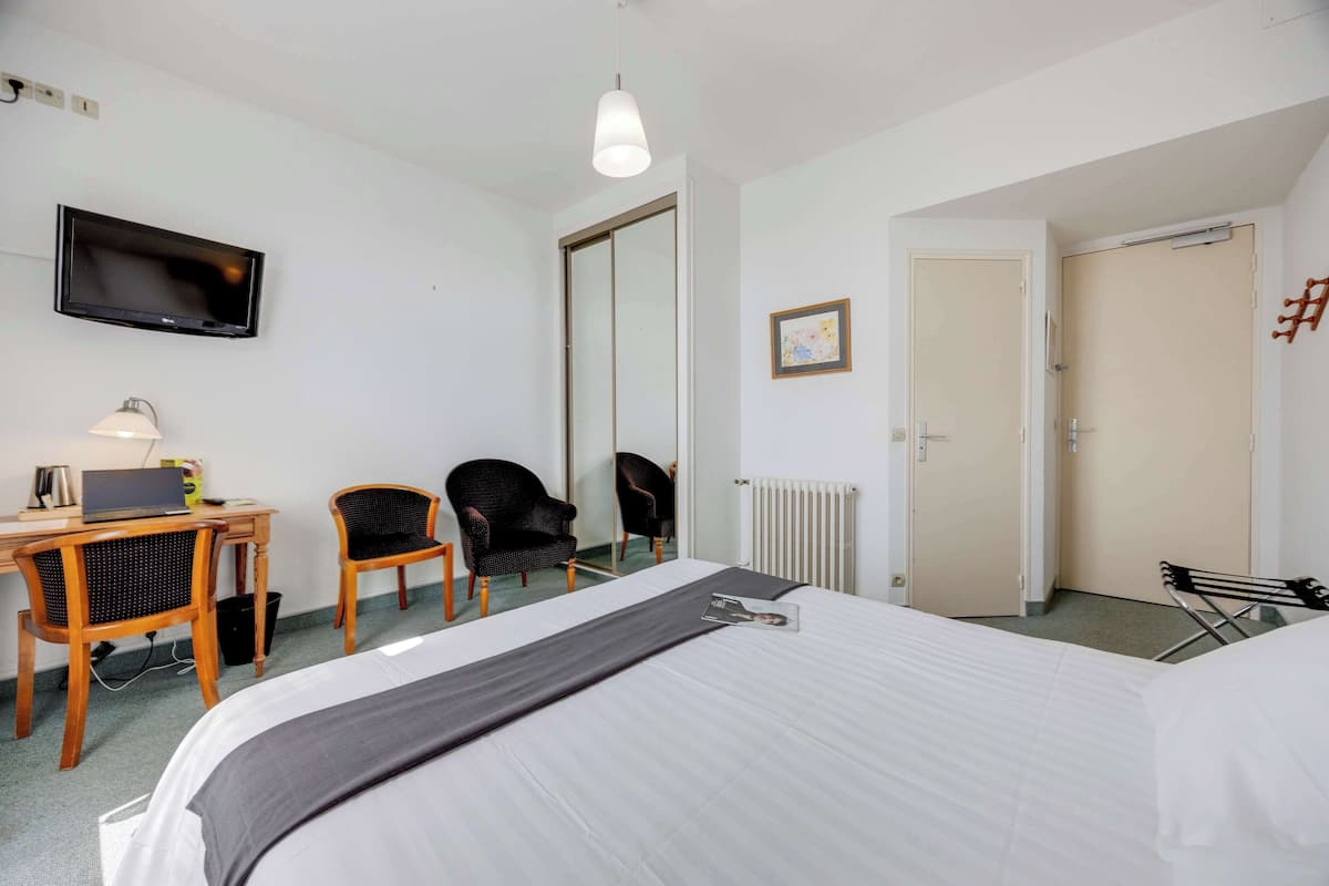Een hotelkamer met een bed, een bureau met een laptop, een stoel, een televisie en een radiator.