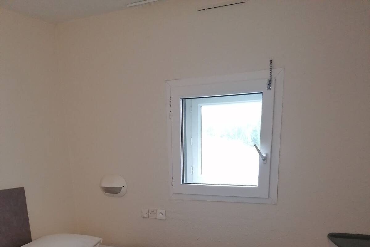 A small room with two beds, a window, a desk, and a chair.
