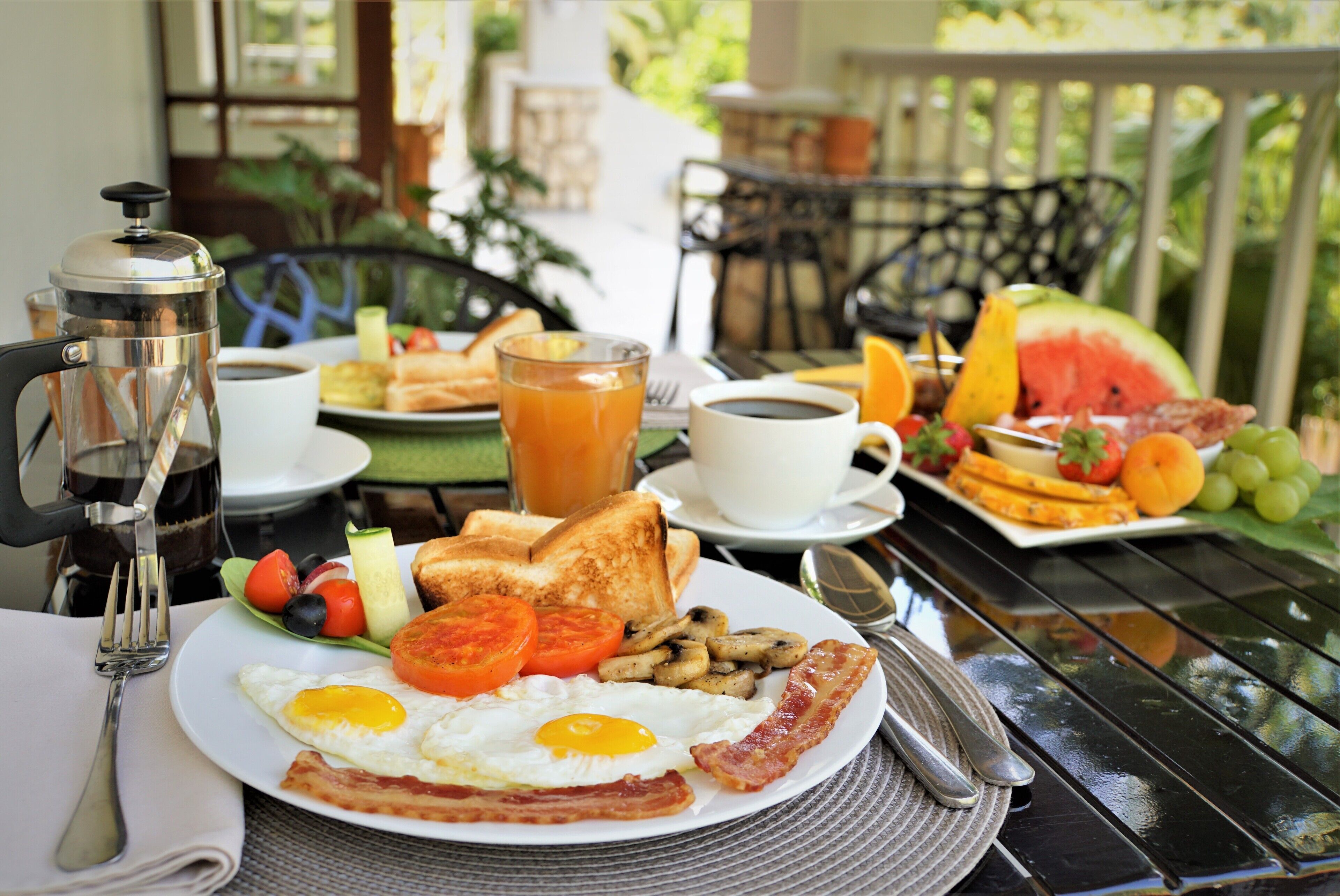 A breakfast table with a variety of foods including toast, eggs, bacon, tomatoes, and a glass of orange juice.