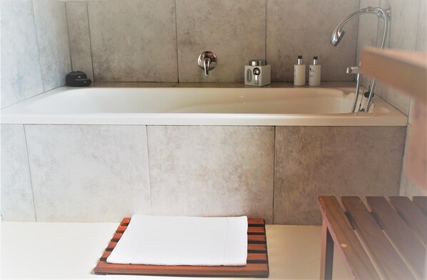 A bathroom with a bathtub, a wooden bench, and a towel. - Swellendam Country Lodge (Swellendam)