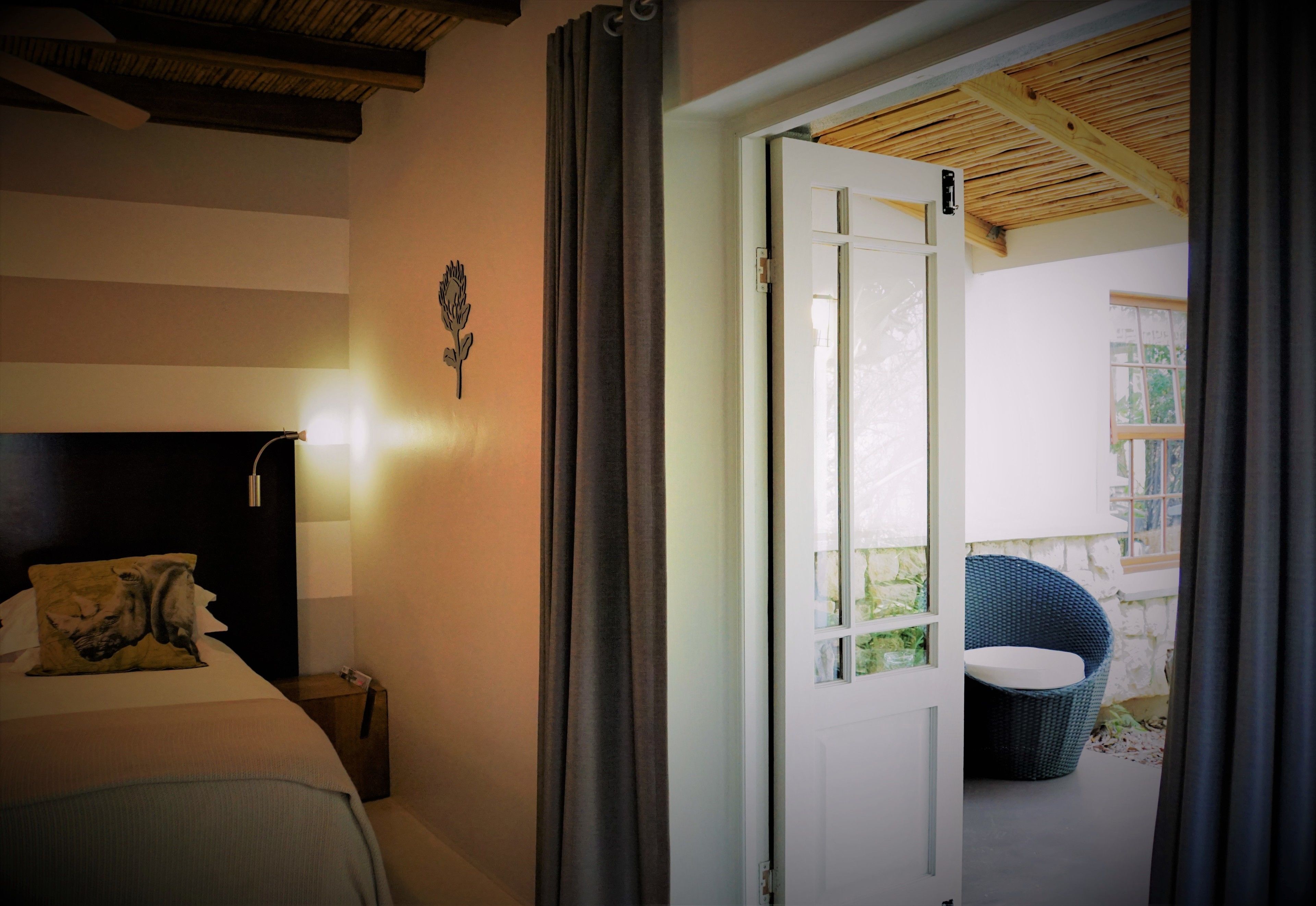 Ein Schlafzimmer mit Bett, Nachttisch, Wandlampe und Blick auf einen Außenbereich durch eine geöffnete Tür.