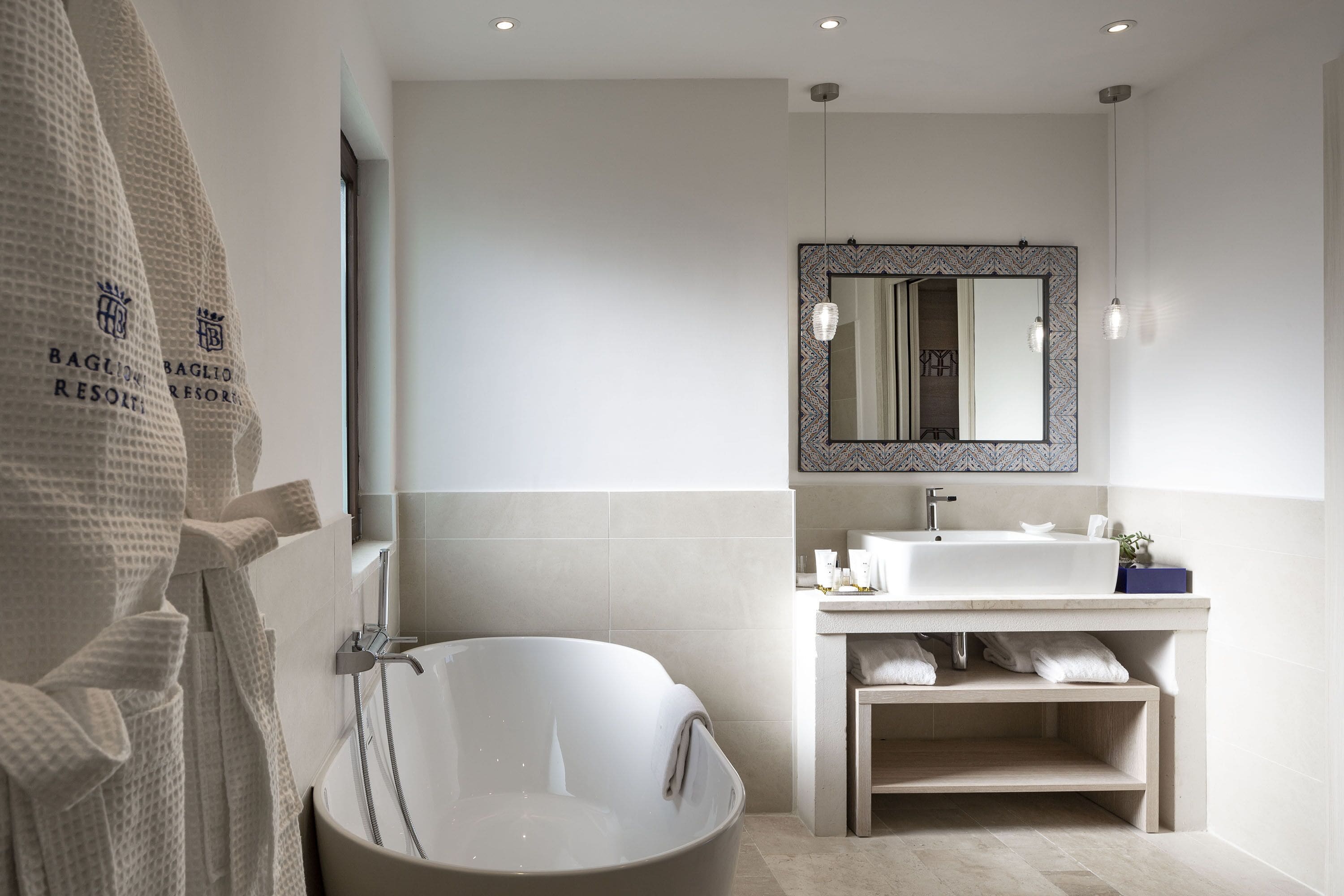 A modern bathroom with a freestanding bathtub, a large mirror with a decorative frame, and a vanity with a sink and towel rack.