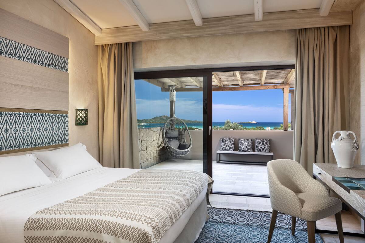 Habitación de hotel con cama, escritorio, silla, sillón colgante y vista al mar.