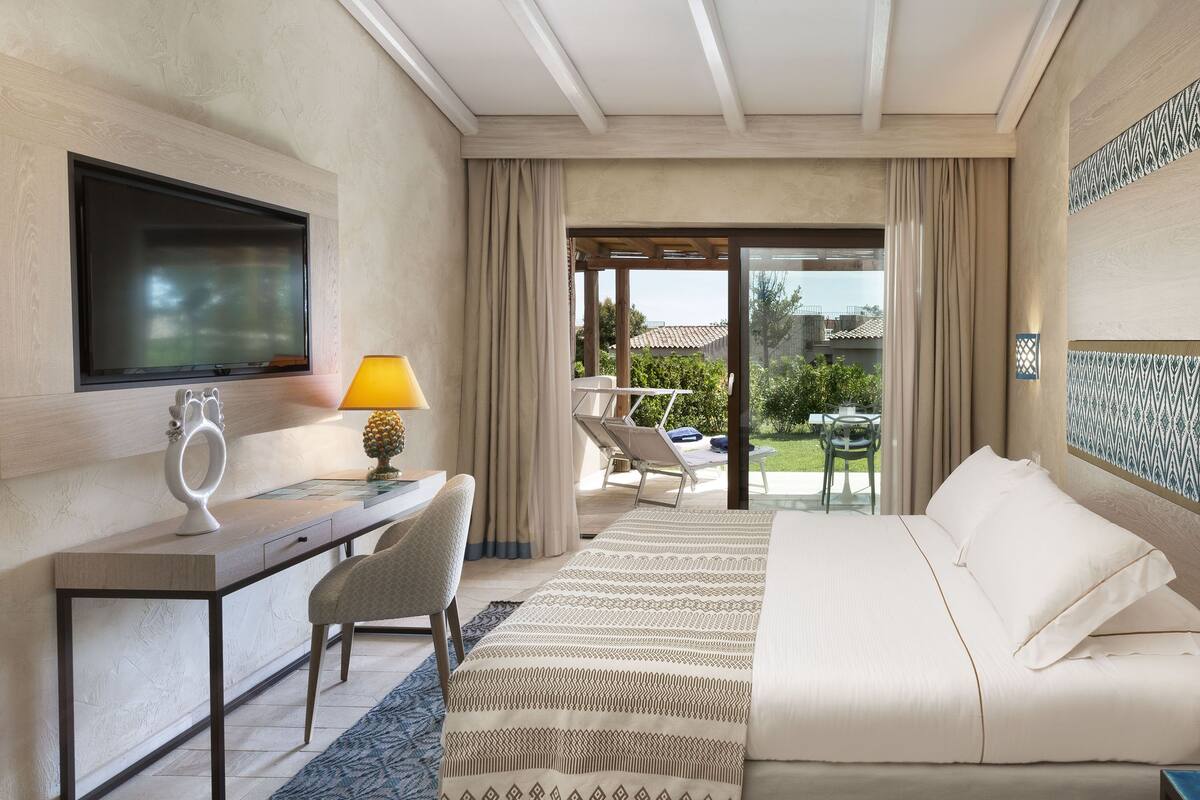 Habitación de hotel con cama, escritorio, silla, televisor y vista al exterior.